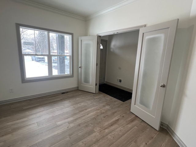 unfurnished bedroom featuring visible vents, ornamental molding, light wood-style flooring, and baseboards