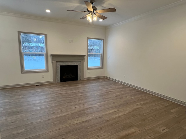 unfurnished living room featuring ceiling fan, wood finished floors, a high end fireplace, baseboards, and crown molding