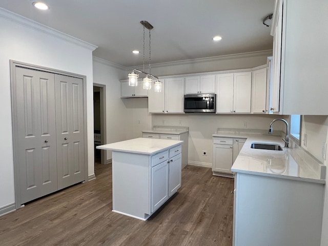 kitchen with a sink, a kitchen island, white cabinets, hanging light fixtures, and stainless steel microwave