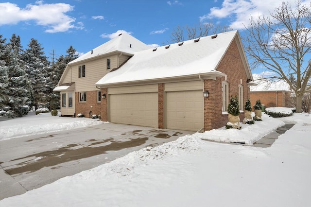 view of snow covered exterior with brick siding and an attached garage