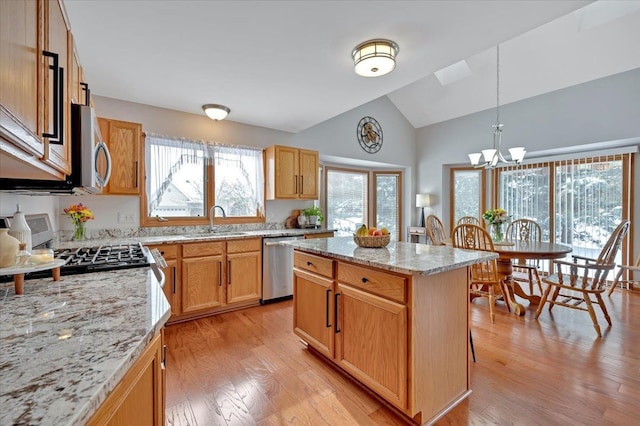 kitchen featuring a sink, a center island, appliances with stainless steel finishes, light stone countertops, and light wood finished floors