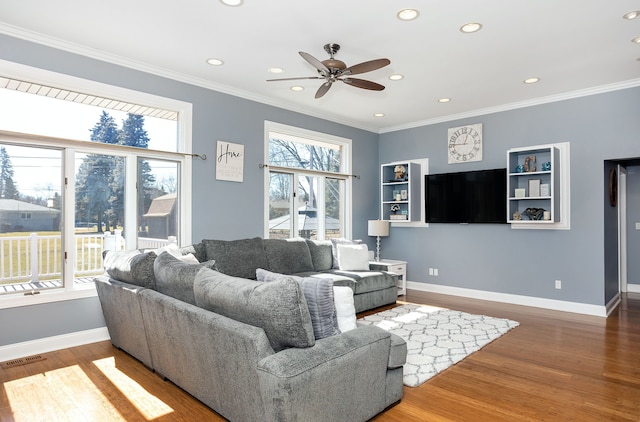 living area with visible vents, baseboards, wood finished floors, and crown molding