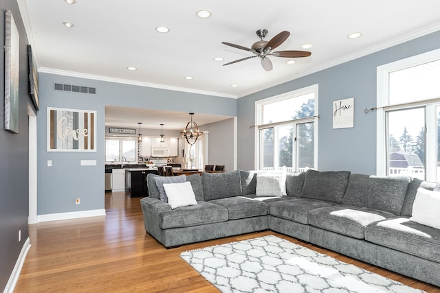 living room featuring crown molding, baseboards, visible vents, and light wood-type flooring