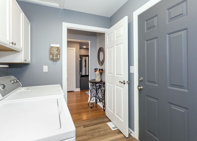 clothes washing area with washer and clothes dryer, cabinet space, baseboards, and wood finished floors