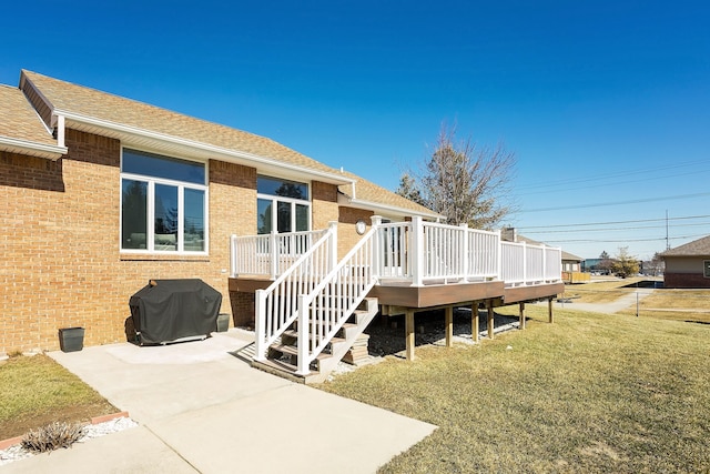 rear view of house featuring roof with shingles, stairs, a deck, a lawn, and brick siding