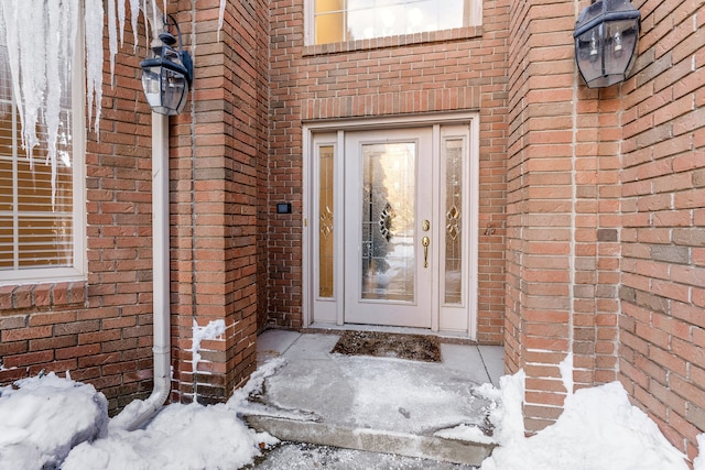 snow covered property entrance with brick siding