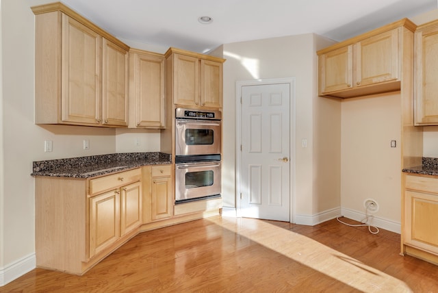 kitchen featuring double oven, light brown cabinets, light wood finished floors, and dark stone countertops