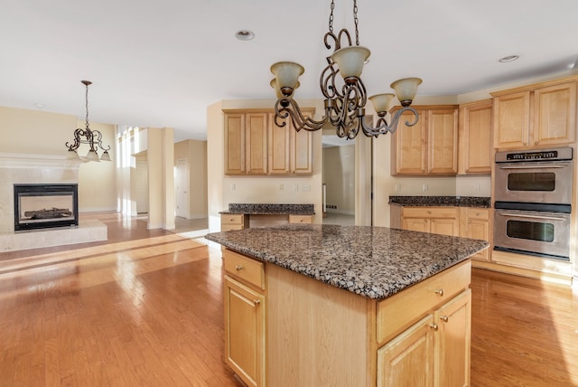 kitchen with double oven, a kitchen island, an inviting chandelier, and light brown cabinetry