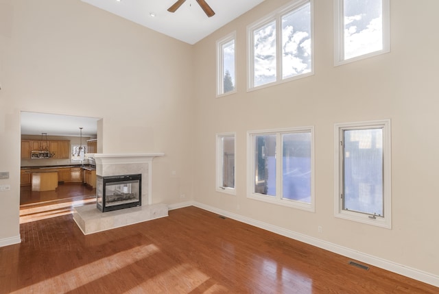 unfurnished living room with a towering ceiling, dark wood-style floors, baseboards, and a high end fireplace