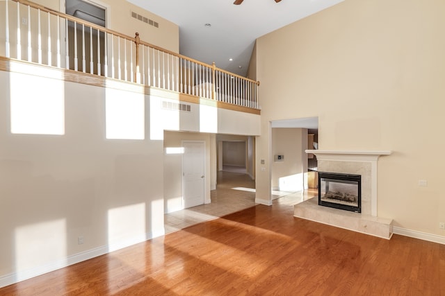 unfurnished living room with a high ceiling, visible vents, wood finished floors, and a high end fireplace