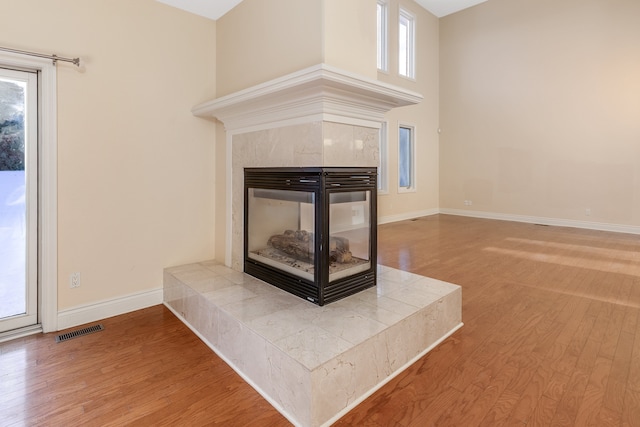 interior space featuring a tile fireplace, visible vents, baseboards, and wood finished floors