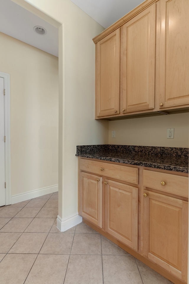 kitchen featuring baseboards, light tile patterned flooring, dark stone countertops, and light brown cabinetry