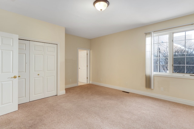 unfurnished bedroom featuring a closet, light carpet, visible vents, and baseboards