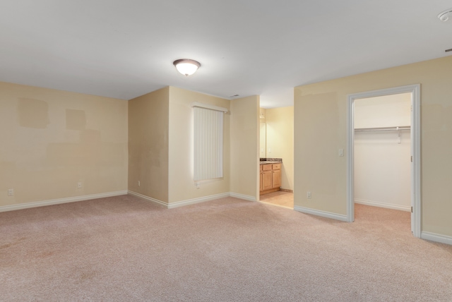 unfurnished bedroom featuring a closet, light colored carpet, a spacious closet, ensuite bath, and baseboards