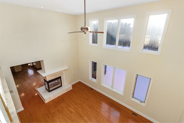 unfurnished living room with baseboards, visible vents, a tile fireplace, ceiling fan, and wood finished floors