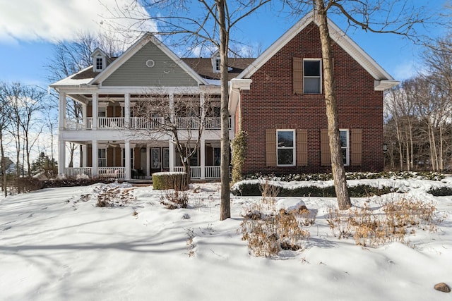 snow covered rear of property with a balcony, a porch, and brick siding