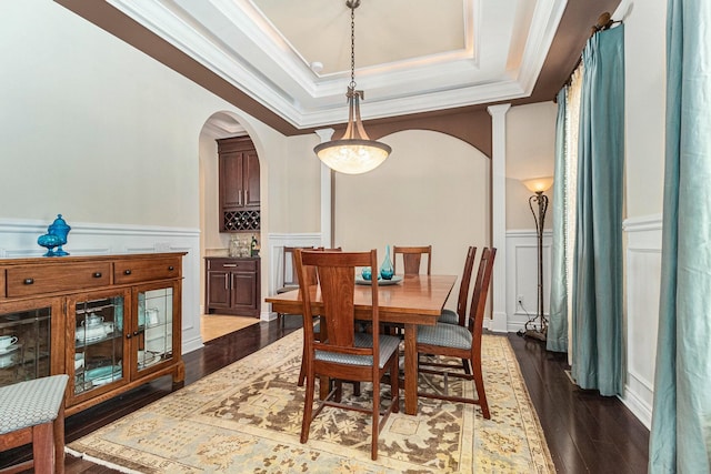 dining room featuring arched walkways, wood finished floors, a wainscoted wall, and a raised ceiling