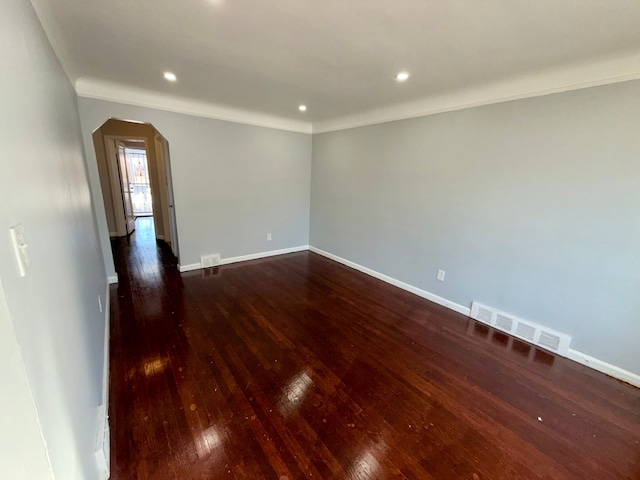 spare room featuring wood-type flooring, visible vents, arched walkways, and baseboards