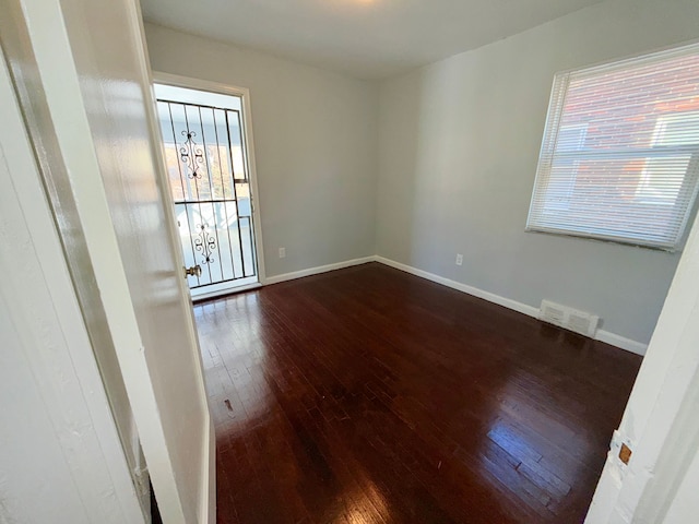 empty room with baseboards, visible vents, and dark wood-style flooring