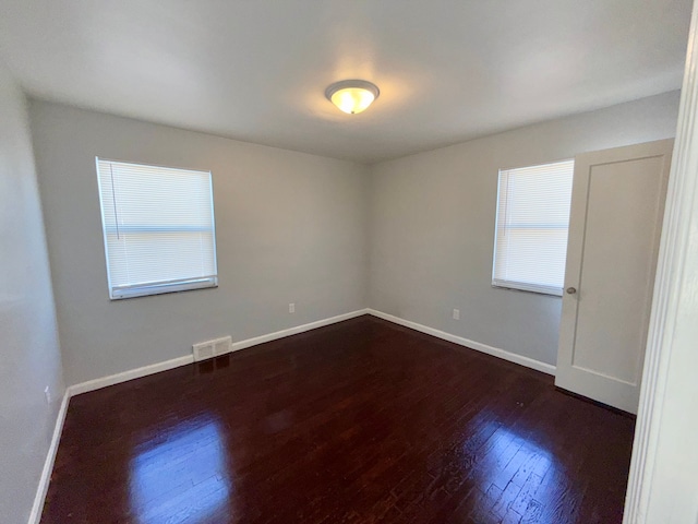 spare room featuring dark wood-style floors, visible vents, and baseboards