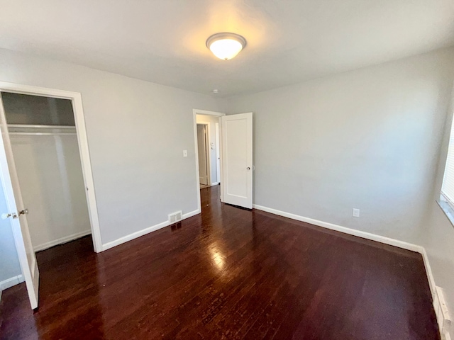 unfurnished bedroom with a closet, visible vents, baseboards, and wood finished floors