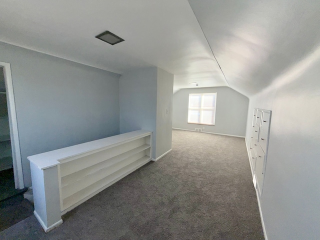 additional living space featuring dark colored carpet, visible vents, vaulted ceiling, and baseboards