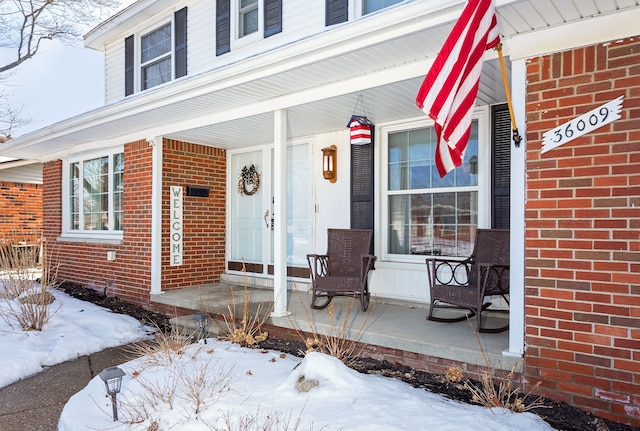 snow covered property entrance with covered porch and brick siding