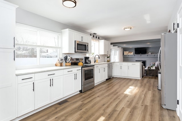 kitchen featuring light wood-style flooring, stainless steel appliances, a sink, white cabinetry, and light countertops