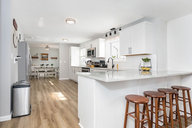 kitchen featuring stainless steel appliances, light stone counters, a peninsula, and white cabinets