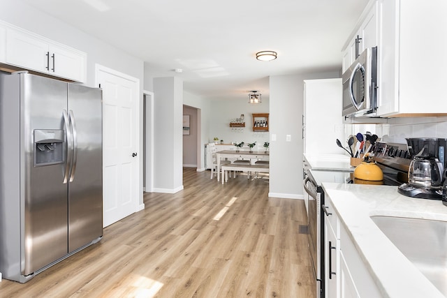 kitchen featuring white cabinets, decorative backsplash, light wood-style flooring, appliances with stainless steel finishes, and light countertops