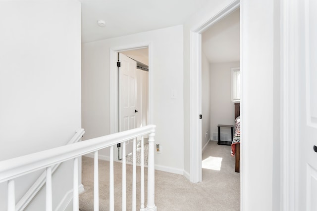 hall featuring baseboards, light carpet, visible vents, and an upstairs landing