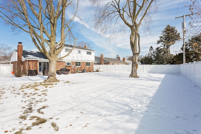 snow covered rear of property featuring a fenced backyard and brick siding