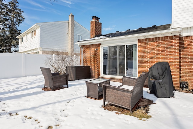 snow covered house with a chimney, fence, and brick siding