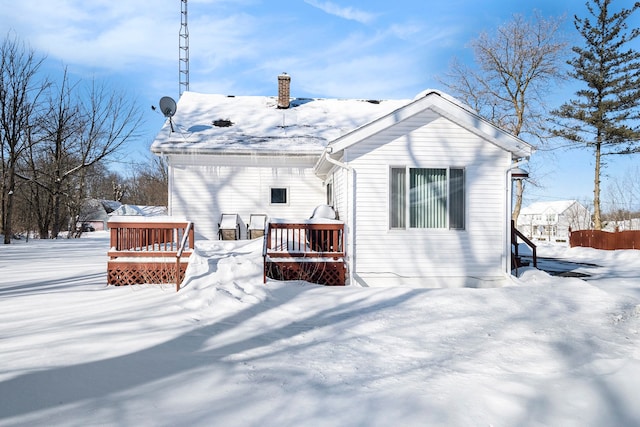 snow covered house with a chimney and a wooden deck