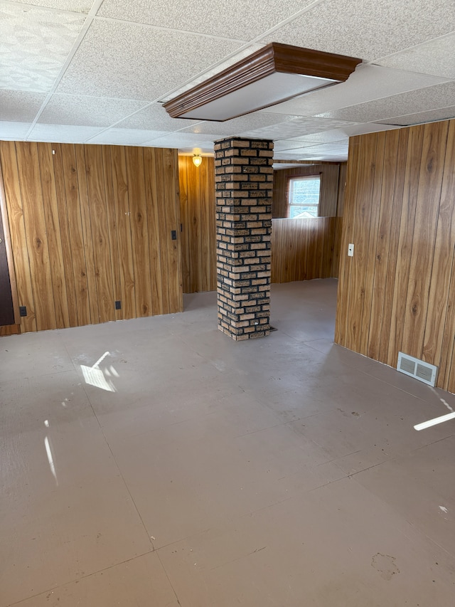 basement featuring a paneled ceiling and wood walls