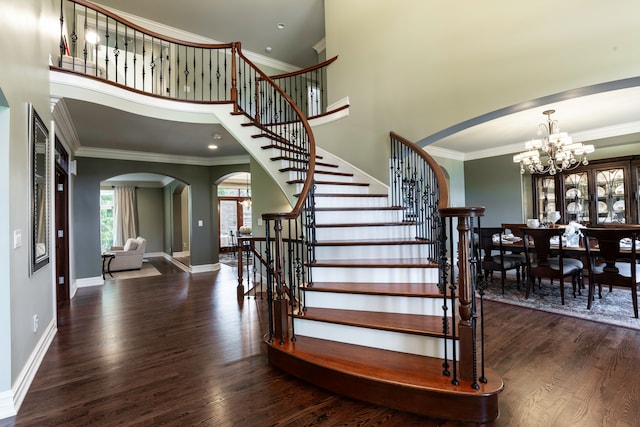 stairs with a notable chandelier, crown molding, a towering ceiling, and hardwood / wood-style floors