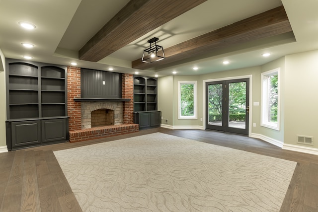 unfurnished living room with dark hardwood / wood-style flooring, beamed ceiling, built in shelves, and a brick fireplace