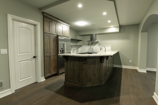 kitchen featuring wall chimney range hood, stainless steel fridge with ice dispenser, dark hardwood / wood-style flooring, a kitchen bar, and kitchen peninsula