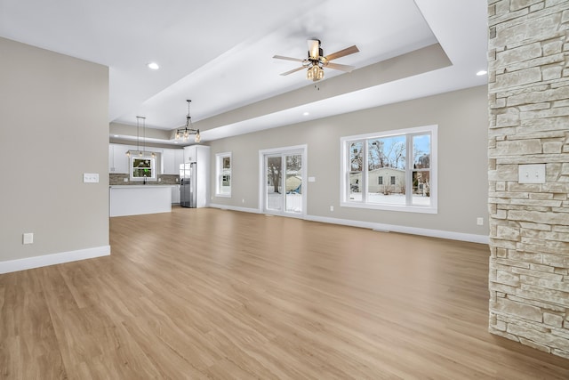 unfurnished living room with a tray ceiling, ceiling fan, and light wood-type flooring