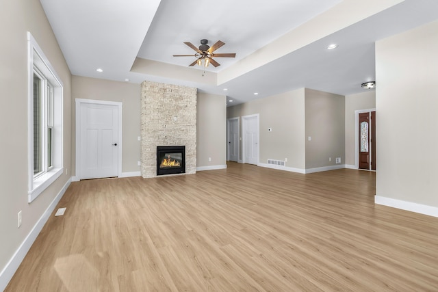 unfurnished living room featuring a tray ceiling, ceiling fan, a fireplace, and light hardwood / wood-style floors