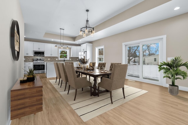 dining room with light wood-type flooring, a raised ceiling, and an inviting chandelier