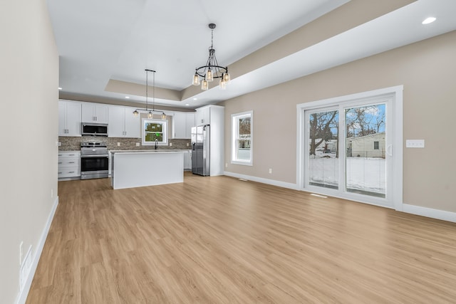 kitchen featuring white cabinetry, a tray ceiling, stainless steel appliances, hanging light fixtures, and tasteful backsplash