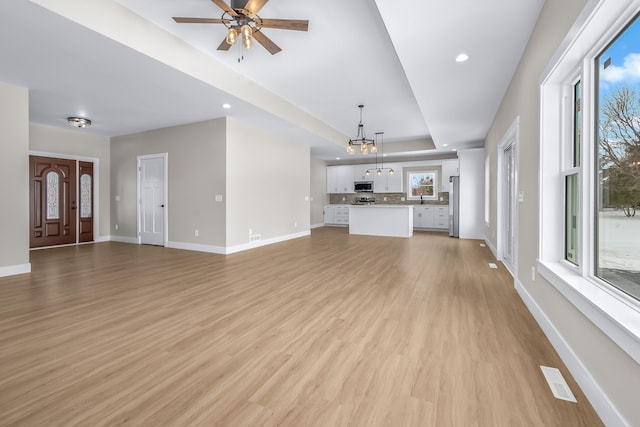 unfurnished living room featuring ceiling fan with notable chandelier, light hardwood / wood-style floors, and a raised ceiling