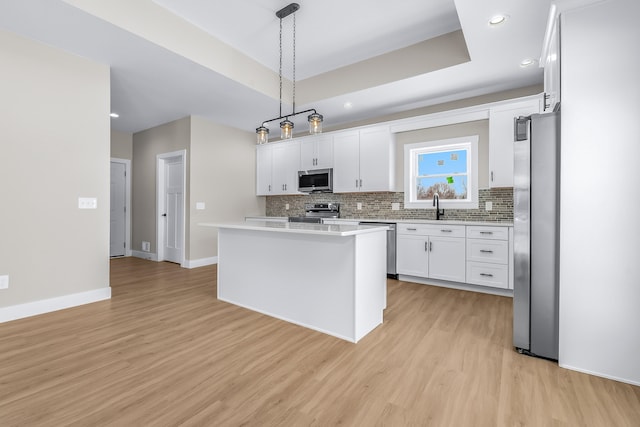 kitchen featuring white cabinetry, a tray ceiling, pendant lighting, a kitchen island, and stainless steel appliances