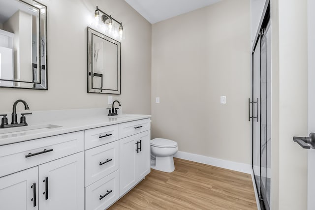 bathroom with toilet, vanity, hardwood / wood-style floors, and a shower with door