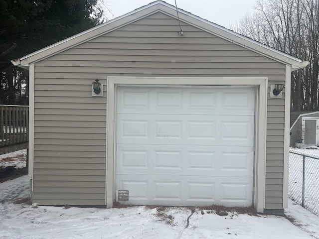 snow covered garage with a garage and fence