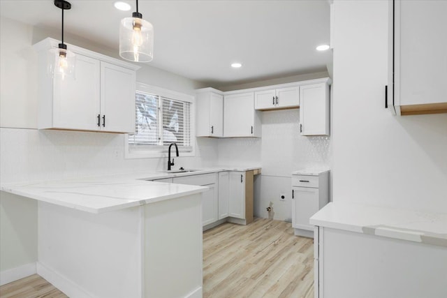 kitchen with white cabinets, light wood-type flooring, pendant lighting, and sink