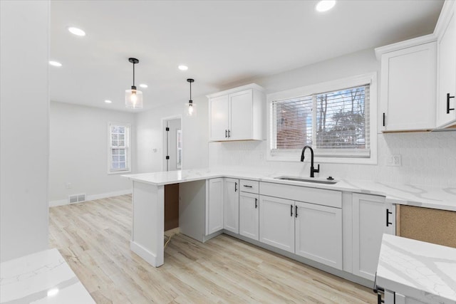 kitchen with kitchen peninsula, decorative light fixtures, sink, backsplash, and white cabinets