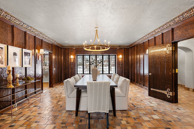 dining area featuring arched walkways, a textured ceiling, brick floor, wooden walls, and a notable chandelier