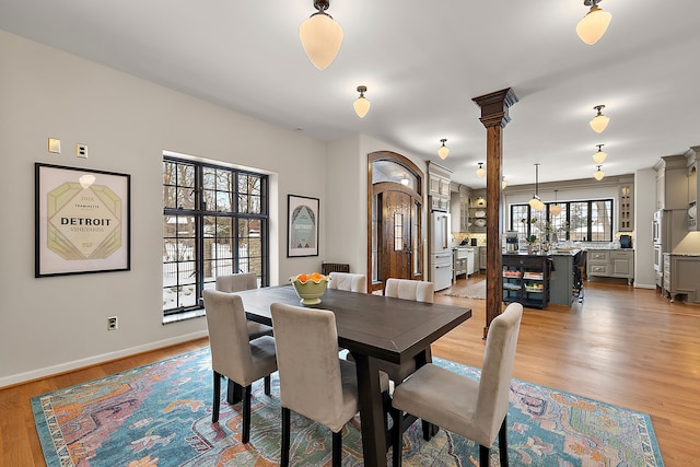 dining room featuring decorative columns, baseboards, and light wood-style flooring